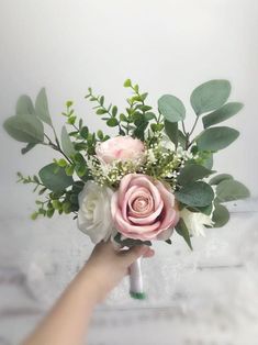 a person holding a pink and white flower bouquet in their hand with greenery on it