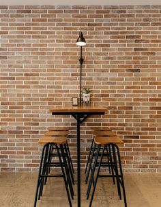 three stools and a table in front of a brick wall with a lamp on it