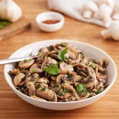 a bowl filled with mushrooms and parsley on top of a wooden table next to garlic