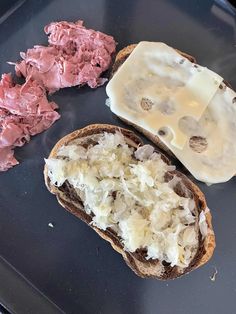 two pieces of bread with meat and cheese on them sitting on a black surface next to other food items