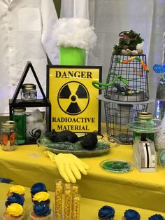 a yellow table topped with cupcakes next to a sign that says danger radioactive material