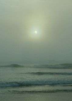 the sun is setting over the ocean on a foggy day