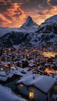 the sun is setting over a small town with mountains in the background and snow on the ground