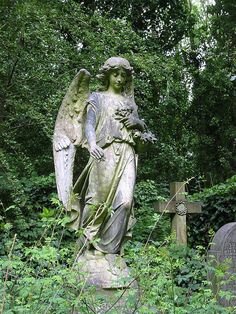 an angel statue sitting in the middle of a cemetery surrounded by green plants and trees