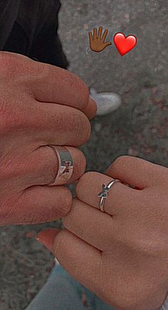 two people holding hands with rings on their fingers and hearts flying above them, in the air