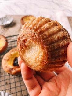 a hand holding a pastry in front of some other pastries on a cooling rack