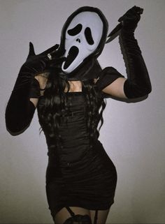 a woman in a black dress with a white mask on her face holding a knife