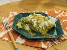 a green plate topped with lasagna covered in cheese and sauce next to a fork