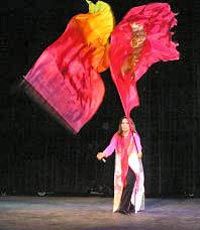 a woman is dancing with red and yellow flags in her hand while she stands on stage