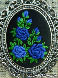 a blue flower embroidered on a black background in an ornate silver frame with filigrees