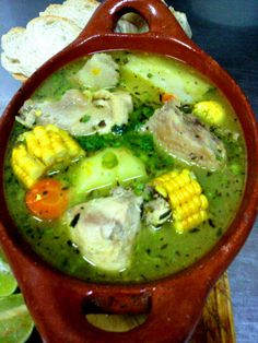 a red bowl filled with soup and corn on the cob next to slices of bread