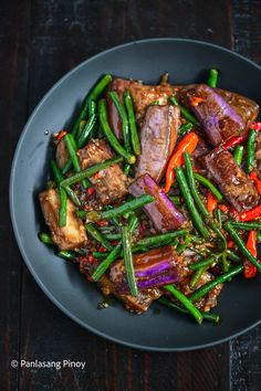 a black plate topped with meat and veggies on top of a wooden table