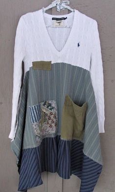 a white sweater with patchwork and pockets hanging on a wooden hanger in front of a door