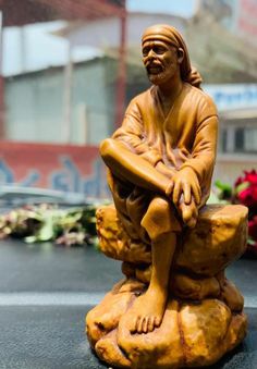 a statue of a man sitting on top of a rock with flowers in the background