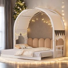 a white bed sitting under a christmas tree next to a window with lights on it