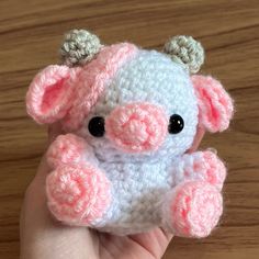 a hand holding a small crocheted pink and white stuffed animal with black eyes