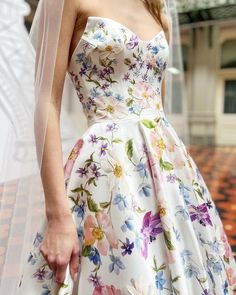 a woman in a floral print dress and veil walks down the street with her hand on her hip