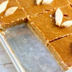 a pan filled with slices of pumpkin pie on top of a wooden table next to a knife