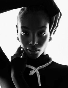 a woman in black and white poses with her hands on her head while wearing a necklace