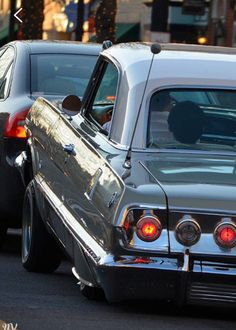 an old car is parked on the side of the road with another car behind it