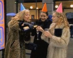 three women standing around each other with wine glasses in their hands and party hats on