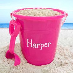 a pink bucket with the word harper written on it sitting in the sand at the beach