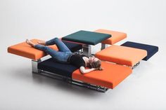 a woman laying on top of an orange and blue couch next to a table with four stools