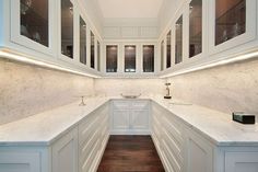 a kitchen with white cabinets and wood flooring, along with marble counter tops on both sides