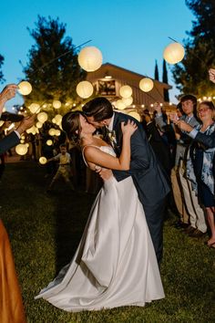 a bride and groom kissing in front of their guests at a wedding reception with paper lanterns overhead