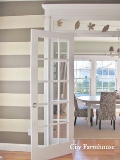 an open door leading to a dining room with striped wallpaper and chairs in it