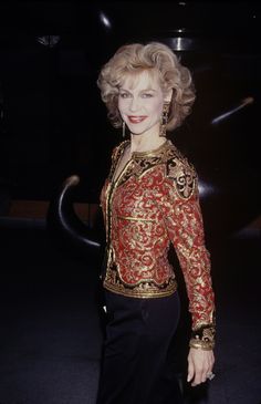 an older woman in a red and gold top posing for a photo with her hands on her hips