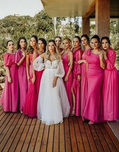 a group of women in pink dresses posing for a photo on a wooden deck with trees in the background