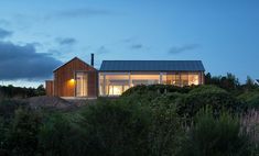 the house is lit up at night on top of a hill with trees and bushes