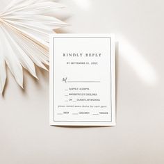 a white wedding response card sitting on top of a table next to a palm leaf