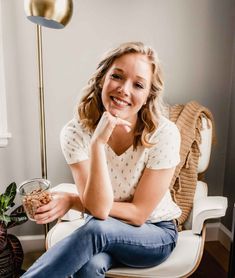 a woman sitting on a chair holding a bowl of food and smiling at the camera