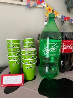 a table topped with green cups filled with soda bottles and monster eyes on the side