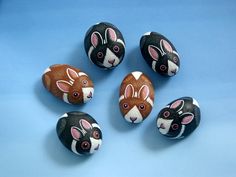 five painted rocks with rabbits on them sitting on a blue surface, one is brown and the other is white