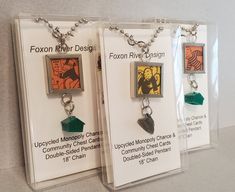 two necklaces with different designs on them in clear plastic cases, one is green and the other is orange