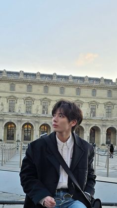 a young man sitting on a bench in front of a building with columns and windows