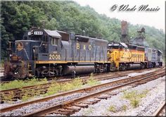 an old train is traveling down the railroad tracks near some trees and bushes in front of a wooded area