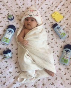 a baby wrapped in a blanket on top of a bed next to bottles and toothbrushes