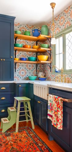 a kitchen with blue cabinets and shelves filled with bowls on top of them, next to a rug