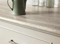 a green coffee pot sitting on top of a counter next to jars and drawers in a kitchen