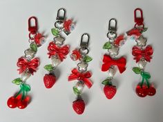 four red and green charms with bows and strawberries hanging from them on a white surface