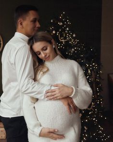 a pregnant couple standing in front of a christmas tree