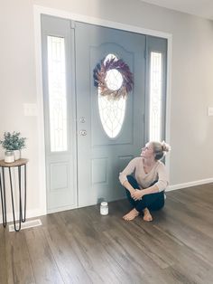 a woman kneeling on the floor in front of a door with a wreath above her head