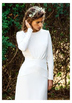 a woman in a white dress is holding her hair up to her ear and wearing a flower crown