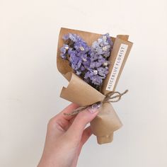 a hand holding a bouquet of lavenders wrapped in brown paper