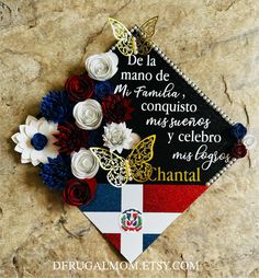 a graduation cap decorated with flowers and butterflies on top of a stone wall in the shape of a flag