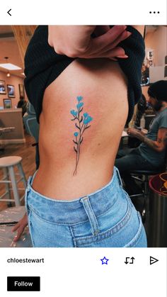 a woman's lower back tattoo with blue flowers on her left side ribcage